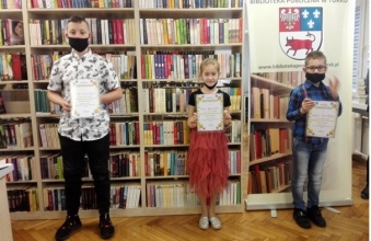 Zdjecie laureatow komkursu z dyplomami w tle regal biblioteczny z ksiazkami