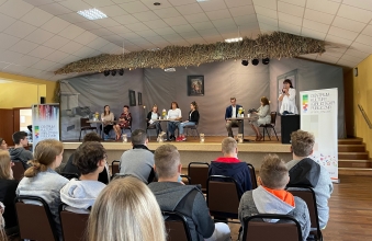 Widok siedzacych uczniowi patrzacych  na scene z czytajacymi lektorami